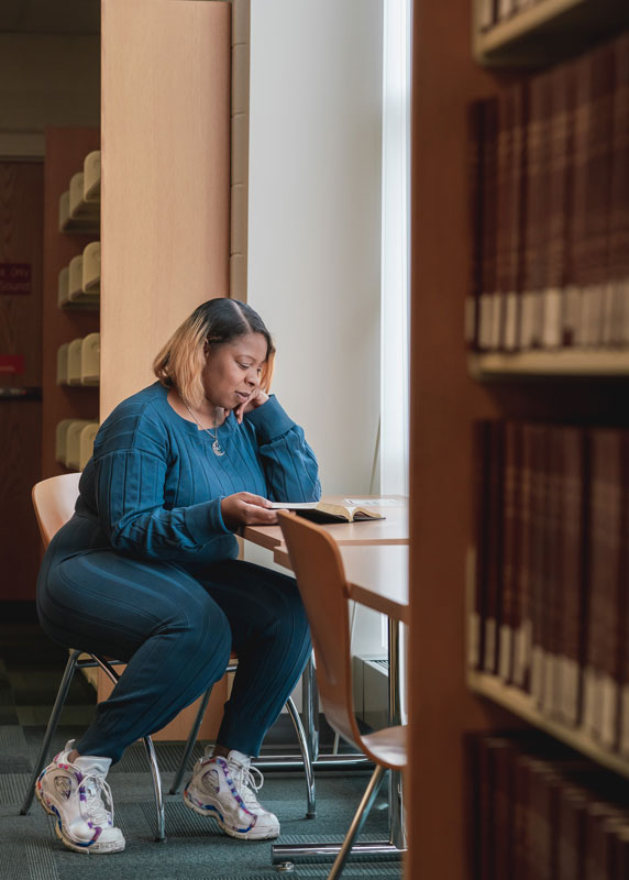 Woman sitting a table near a window reading a book in the library