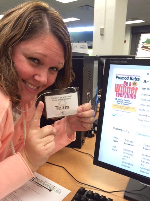 Staff member taking selfie as part of scavenger hunt on library computer looking up a book