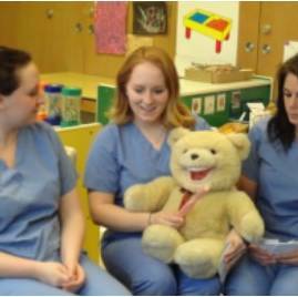 students showing children how to brush their teeth using a bear as demon